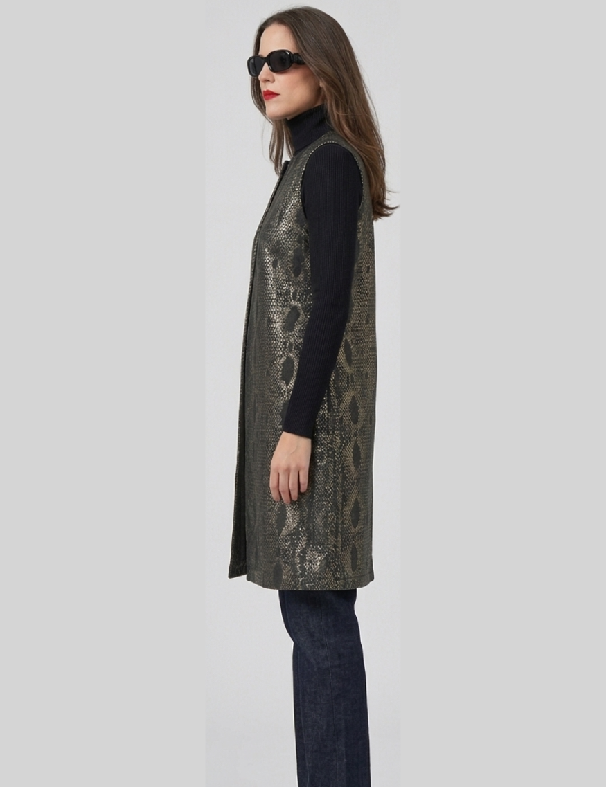 Woman wearing a patterned vest over a black turtleneck and jeans on a light gray background