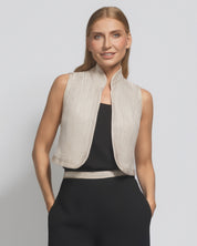 Woman wearing a beige vest over a black top on a light gray background