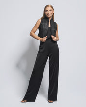 Woman wearing a black sleeveless top and wide-leg pants against a light gray background