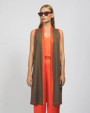 Woman wearing a brown vest over an orange outfit on a plain background