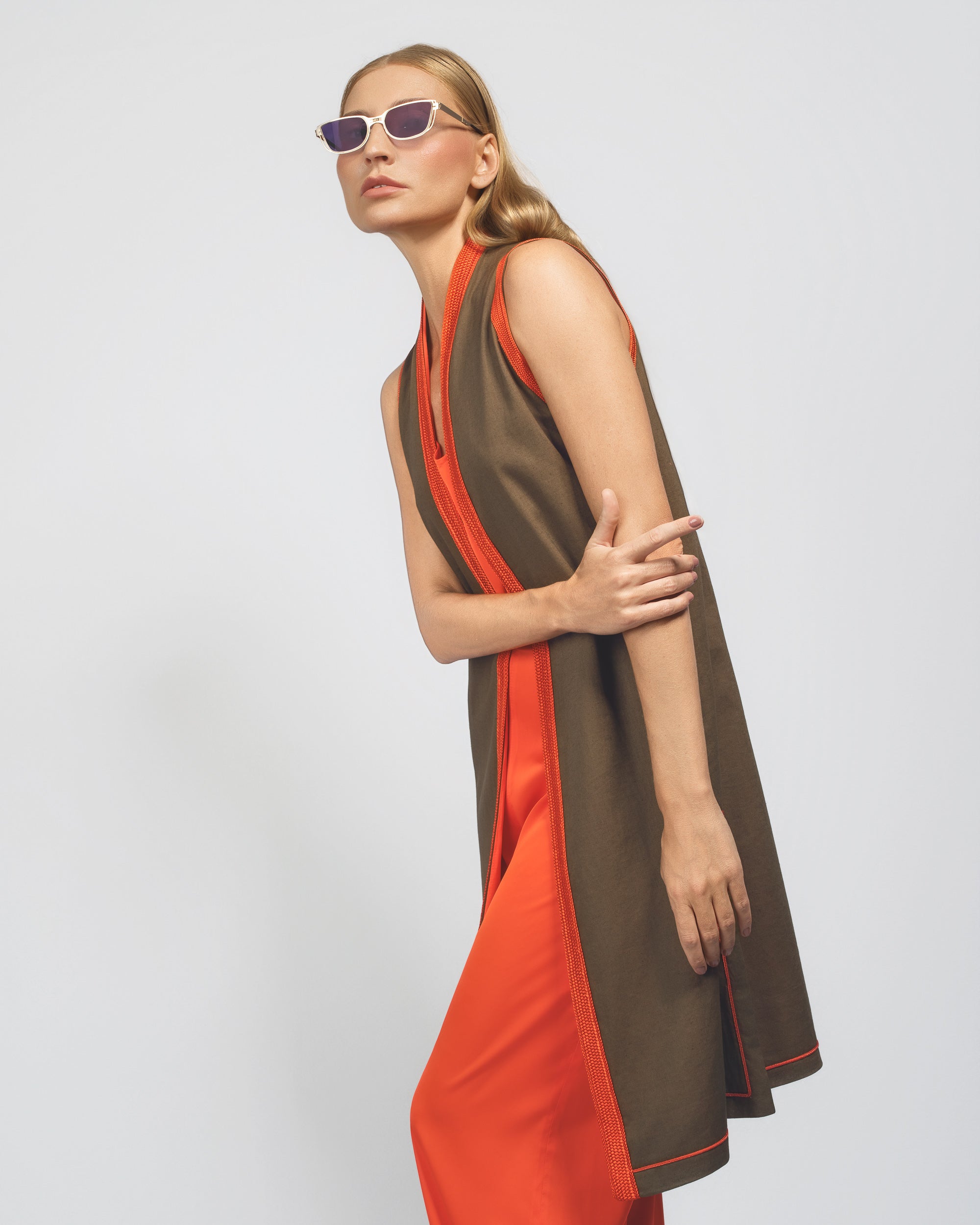 Woman wearing a brown and orange dress with sunglasses on a light gray background