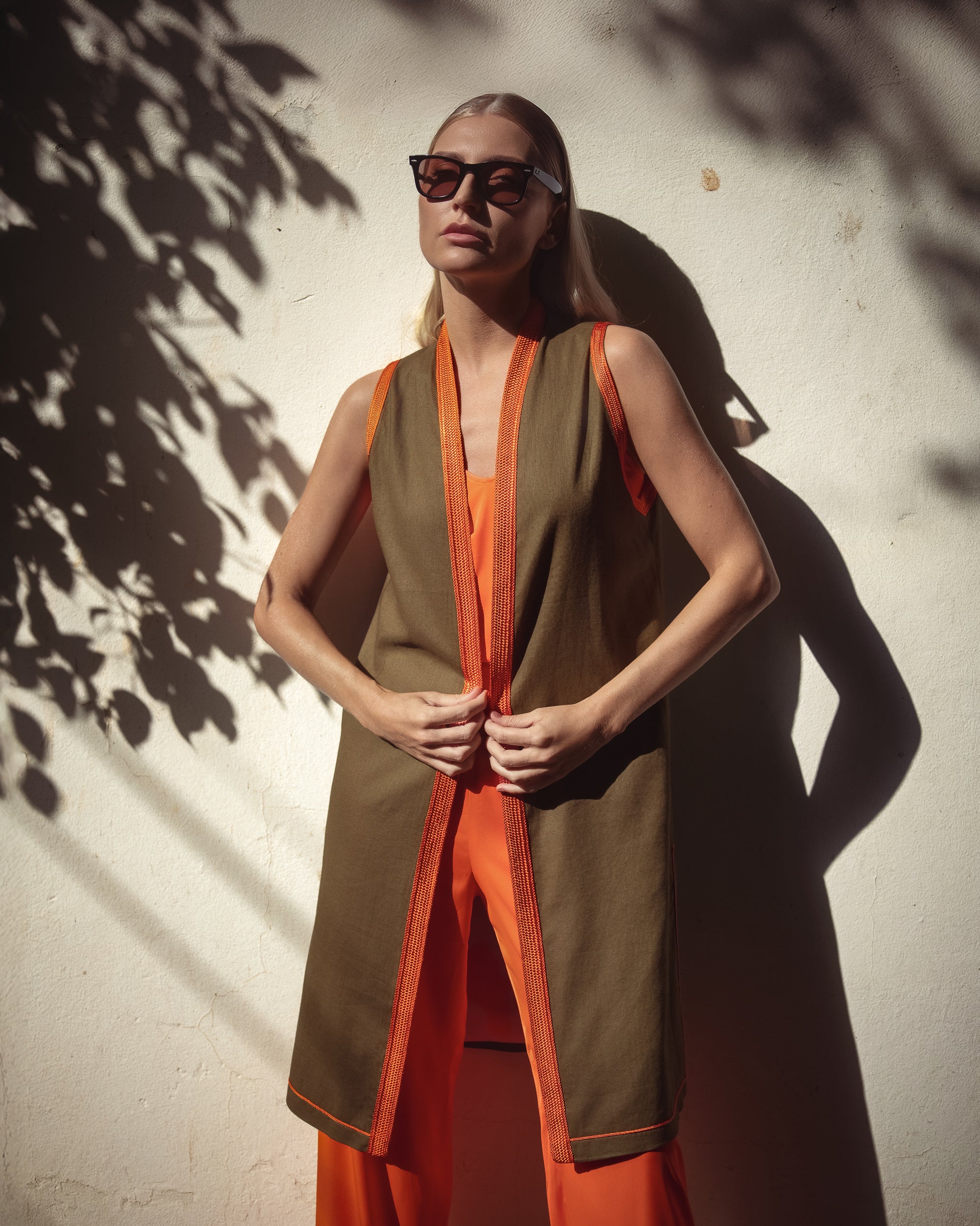 Woman wearing a brown and orange outfit against a textured wall.