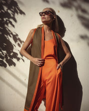 Woman in an orange outfit with a green vest standing against a textured wall.