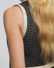 Close-up of a person wearing a black sleeveless top with gold trim and blonde hair.