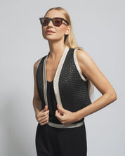Woman wearing a black and beige sleeveless top with sunglasses on a plain background