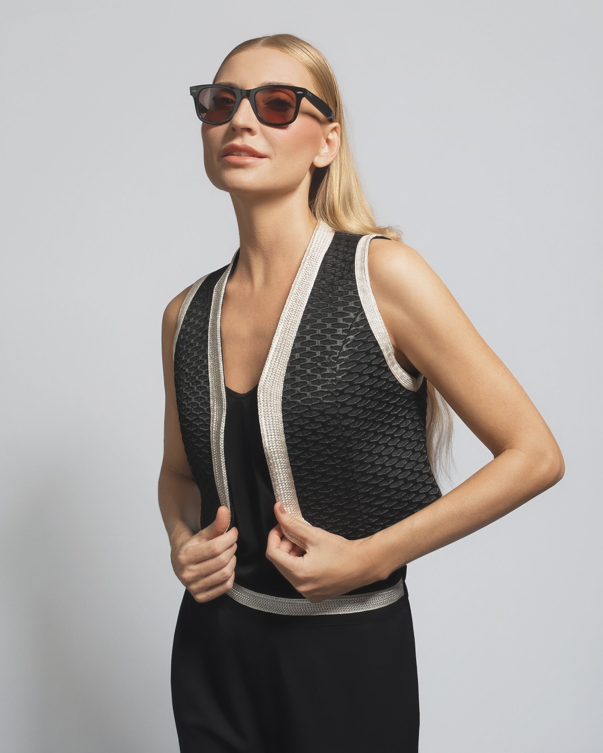 Woman wearing a black and beige sleeveless top with sunglasses on a plain background
