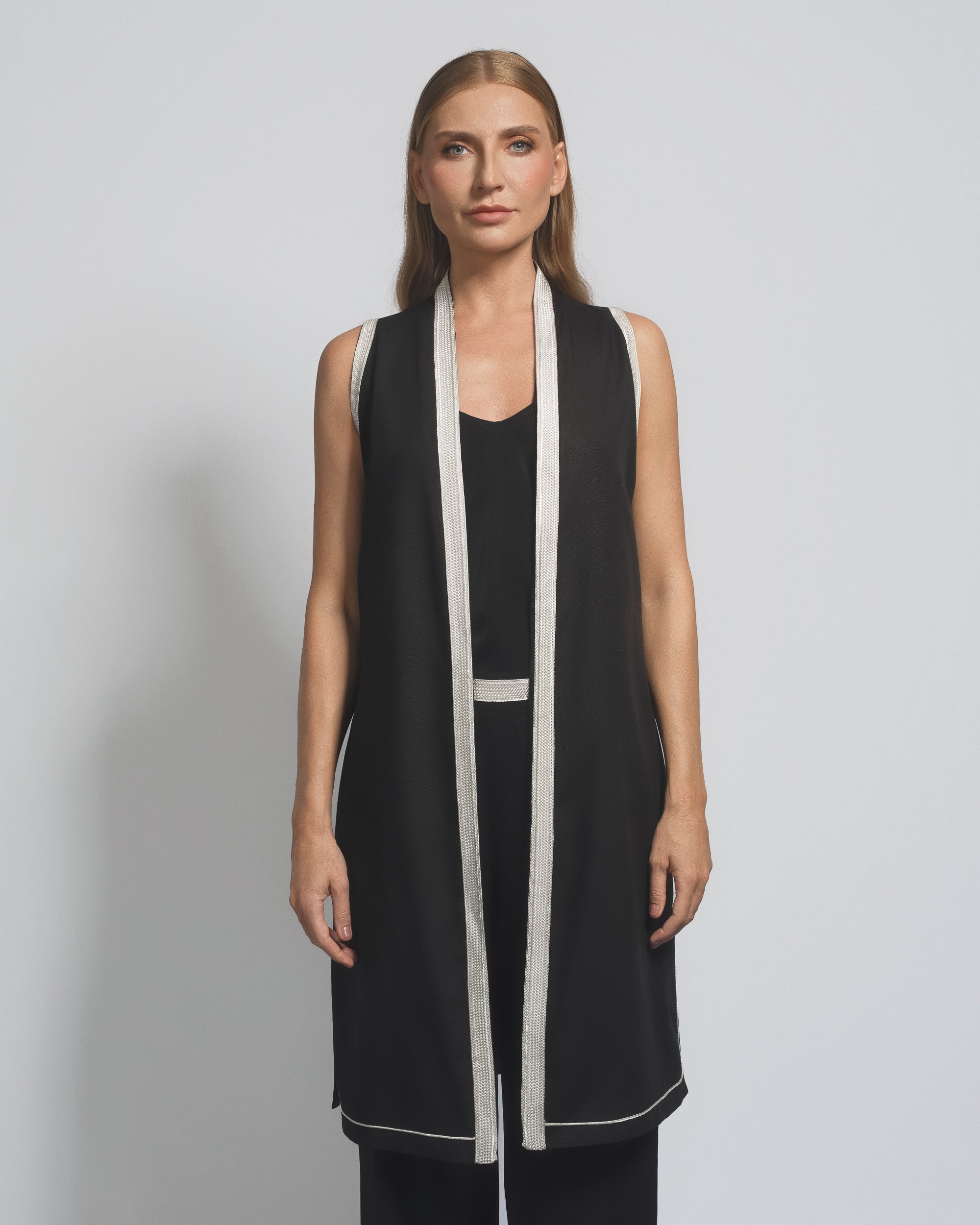 Woman wearing a black sleeveless dress with white trim against a gray background