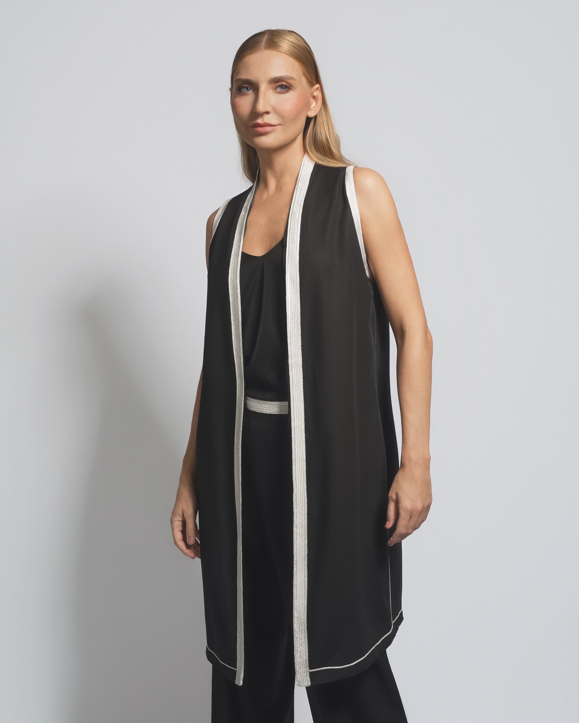 Woman wearing a black sleeveless dress with white trim against a gray background