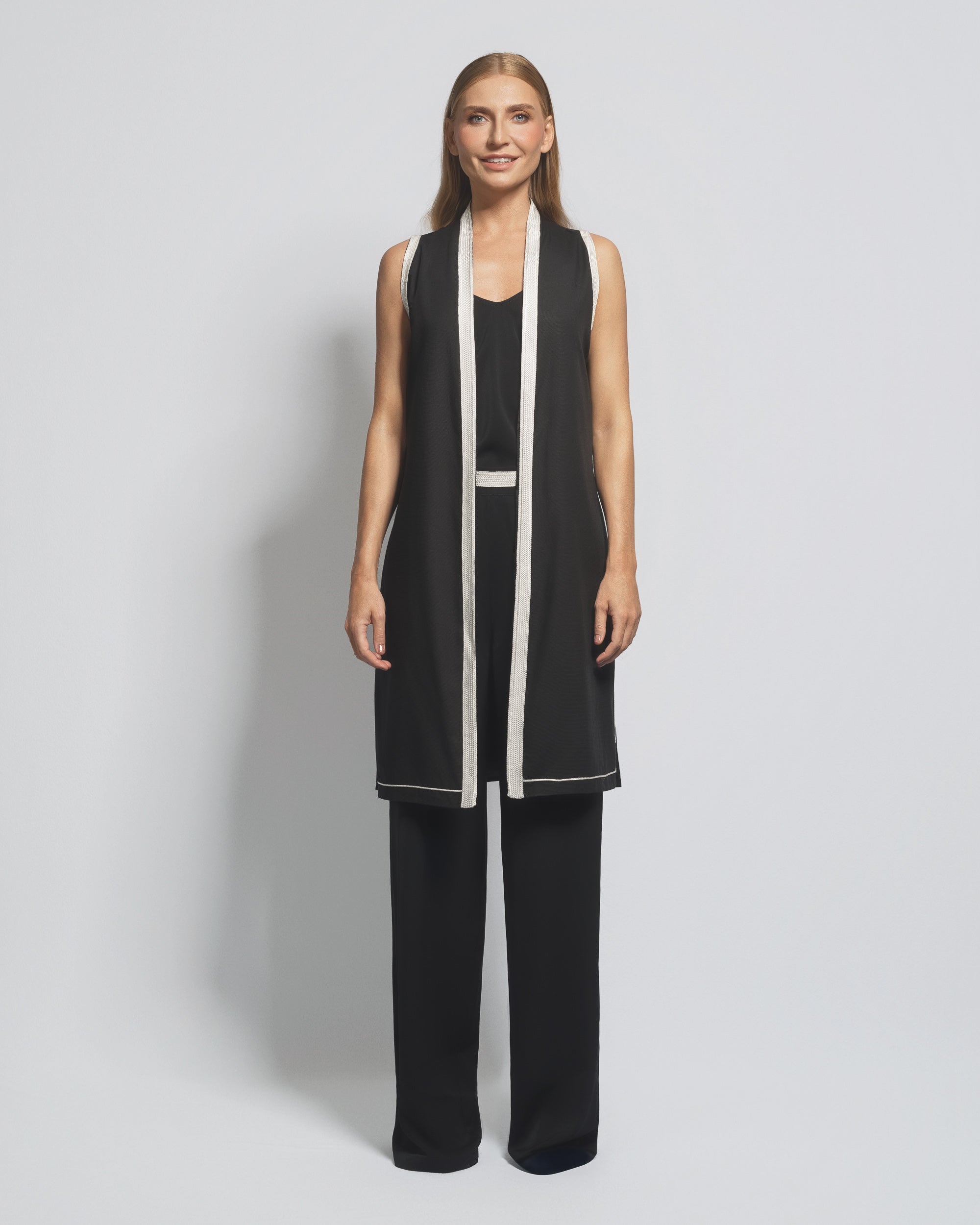 Woman wearing a black and white outfit with a long vest on a gray background