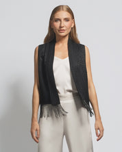 Woman wearing a black fringe vest over a white top and pants on a light gray background