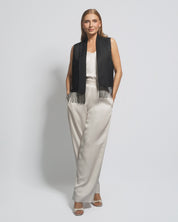 Woman wearing a black vest with fringe and white pants on a light gray background