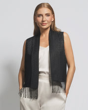 Woman wearing a black vest with fringe details on a plain background