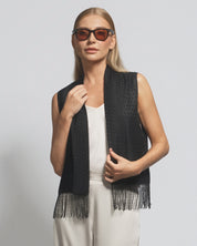 Woman wearing a black fringe vest over a white top on a light gray background