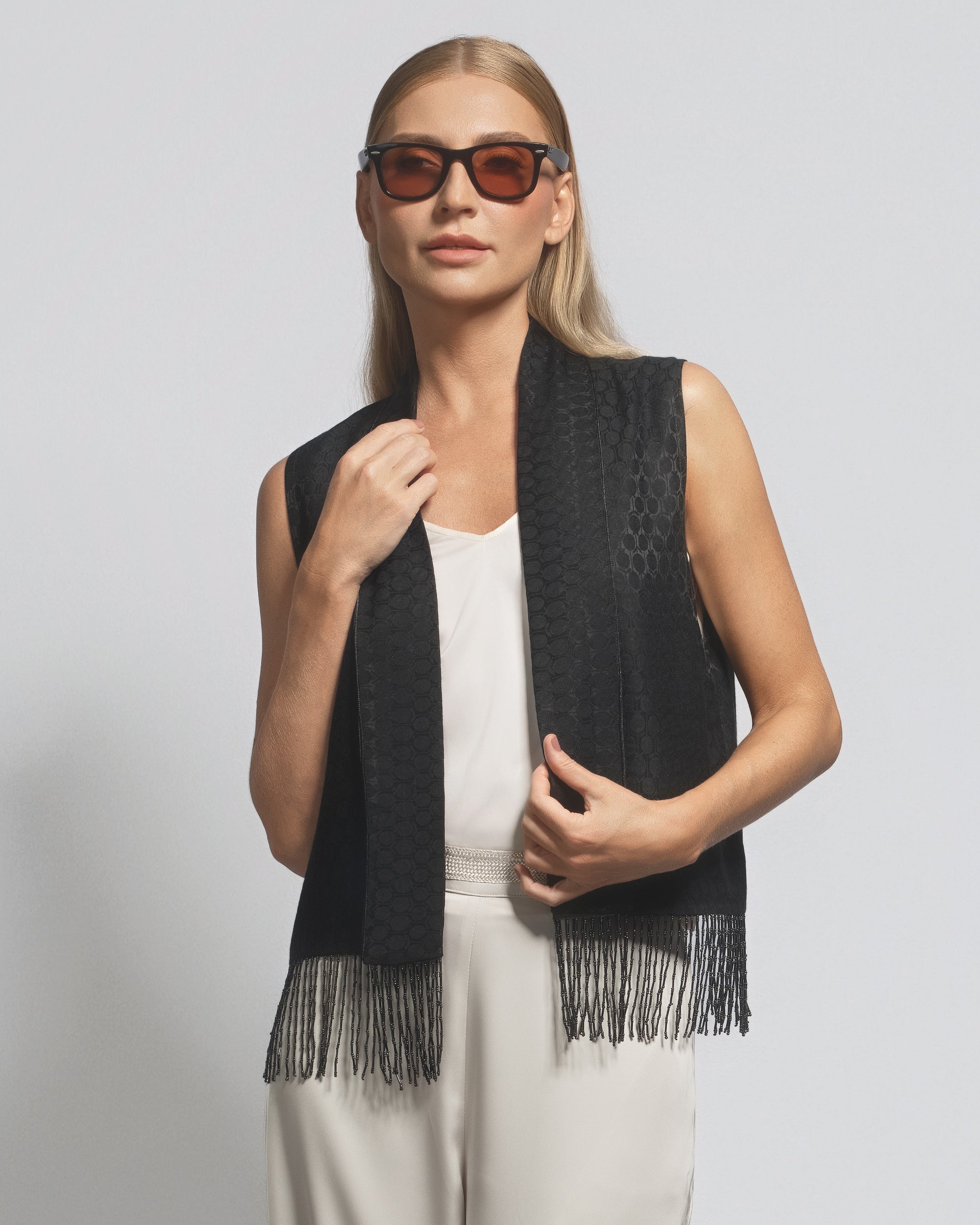 Woman wearing a black fringe vest over a white top on a light gray background