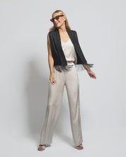 Woman wearing a black vest, white top, and beige pants on a plain background