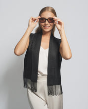 Woman wearing a black scarf with fringe, sunglasses, and a white top against a light gray background