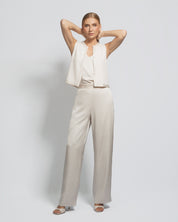 Woman wearing a white sleeveless top and beige pants against a light gray background
