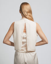 Person wearing a white sleeveless top with cut-out design on a plain background
