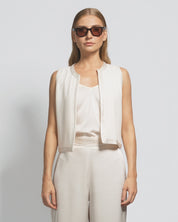 Woman wearing a white sleeveless top and pants with sunglasses on a light gray background