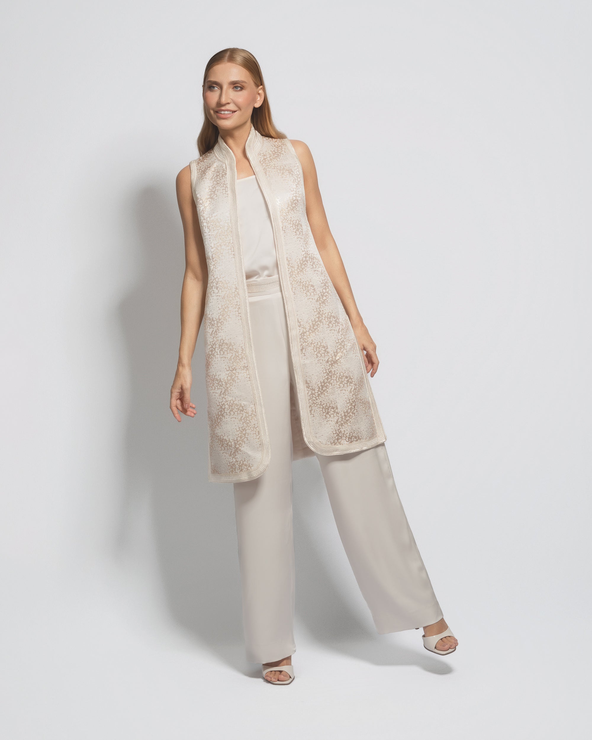 Woman wearing a beige long vest over a white top and light gray pants on a white background