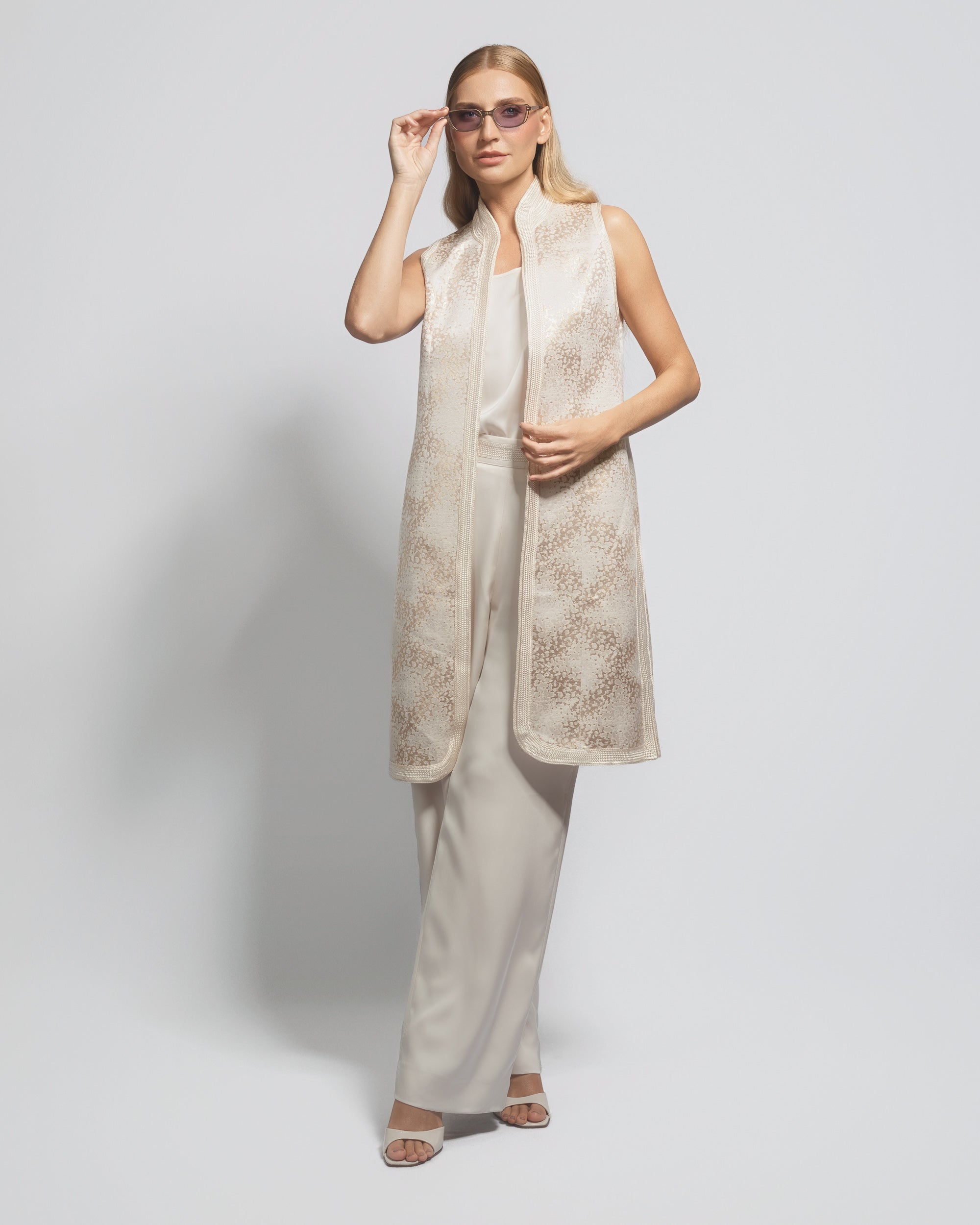 Woman wearing a beige sleeveless top and pants with a matching vest against a white background