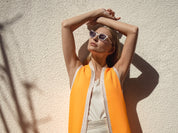 Woman wearing sunglasses and an orange top against a light background