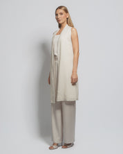Woman wearing a beige sleeveless top and wide-leg pants against a plain background