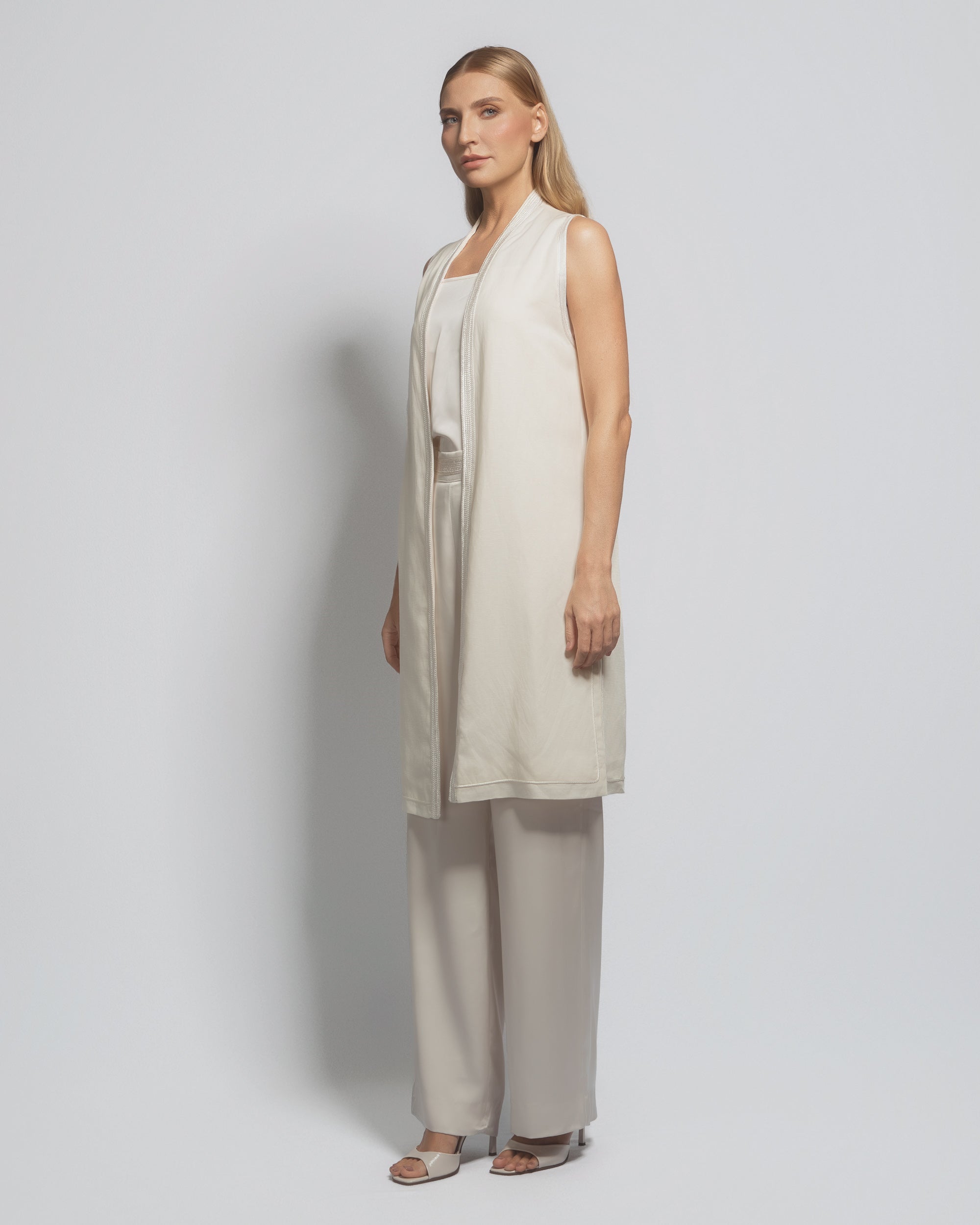 Woman wearing a beige sleeveless top and wide-leg pants against a plain background
