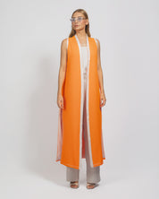 Woman wearing an orange and white long vest over a dress on a white background
