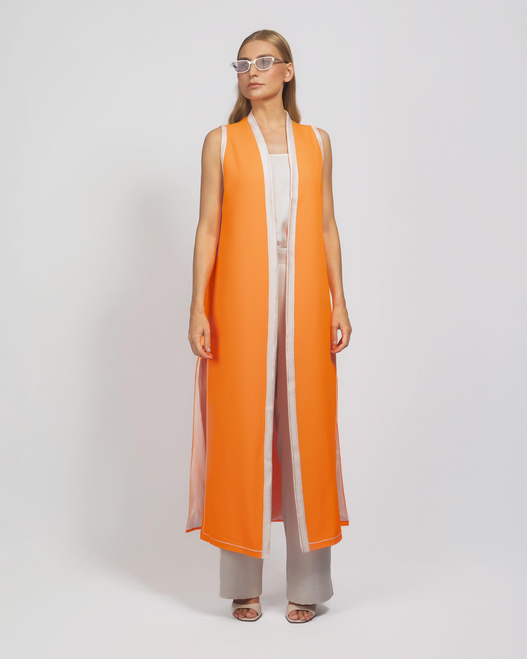 Woman wearing an orange and white long vest over a dress on a white background