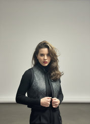 Woman wearing a black vest over a black top against a plain background