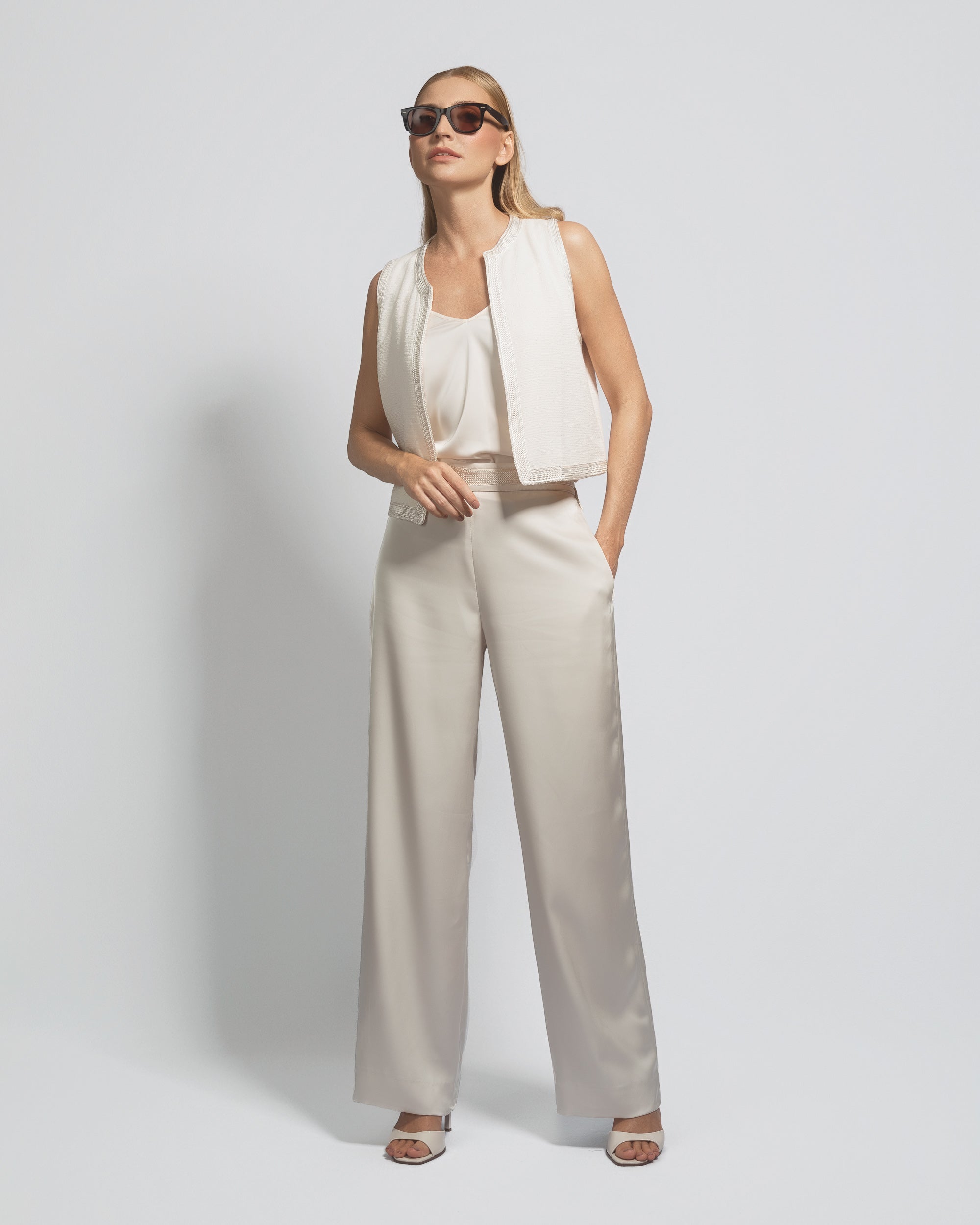 Woman wearing a white sleeveless top and beige wide-leg pants against a light gray background